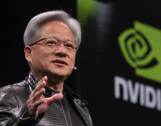 Jensen Huang speaks on stage beside a large Nvidia logo during a technology event.