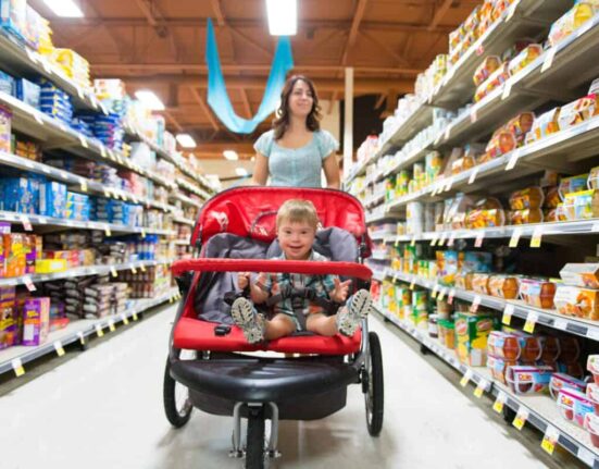A woman shops in a grocery store while pushing a stroller with a child