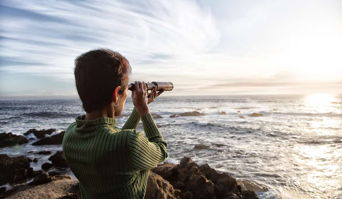 person with spyglass looks at ocean horizon