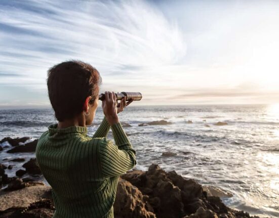 person with spyglass looks at ocean horizon